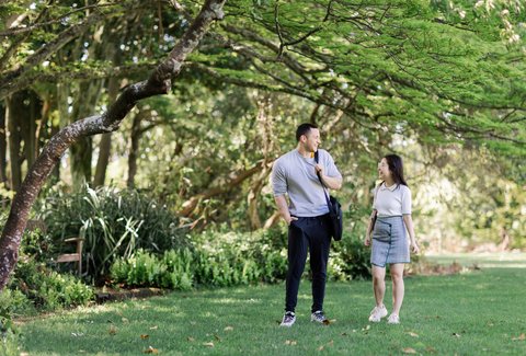 Two people having a conversation on Massey campus with garden and trees behind them.