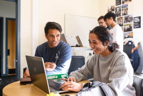 Two students looking at laptop having a conversation.