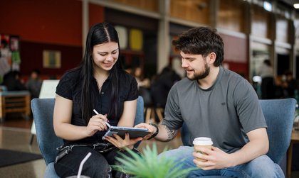 Two students seated and talking in social hub on campus.
