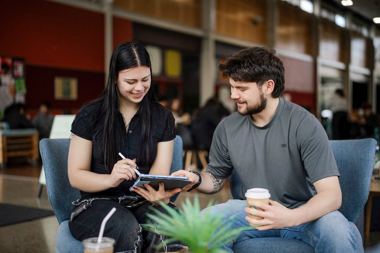 Two students seated and talking in social hub on campus.