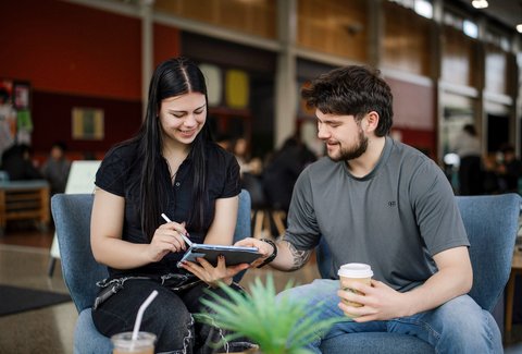Two students seated and talking in social hub on campus.