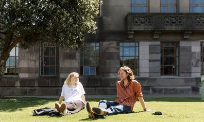 Two students sitting on green lawn outside campus in Wellington.