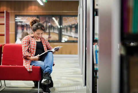 A student sitting in a library reading a book.