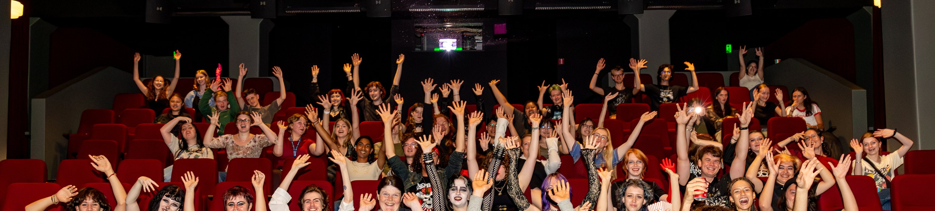 Orientation movie night on Wellington campus. Group of students lifting there arms waving to the camera.